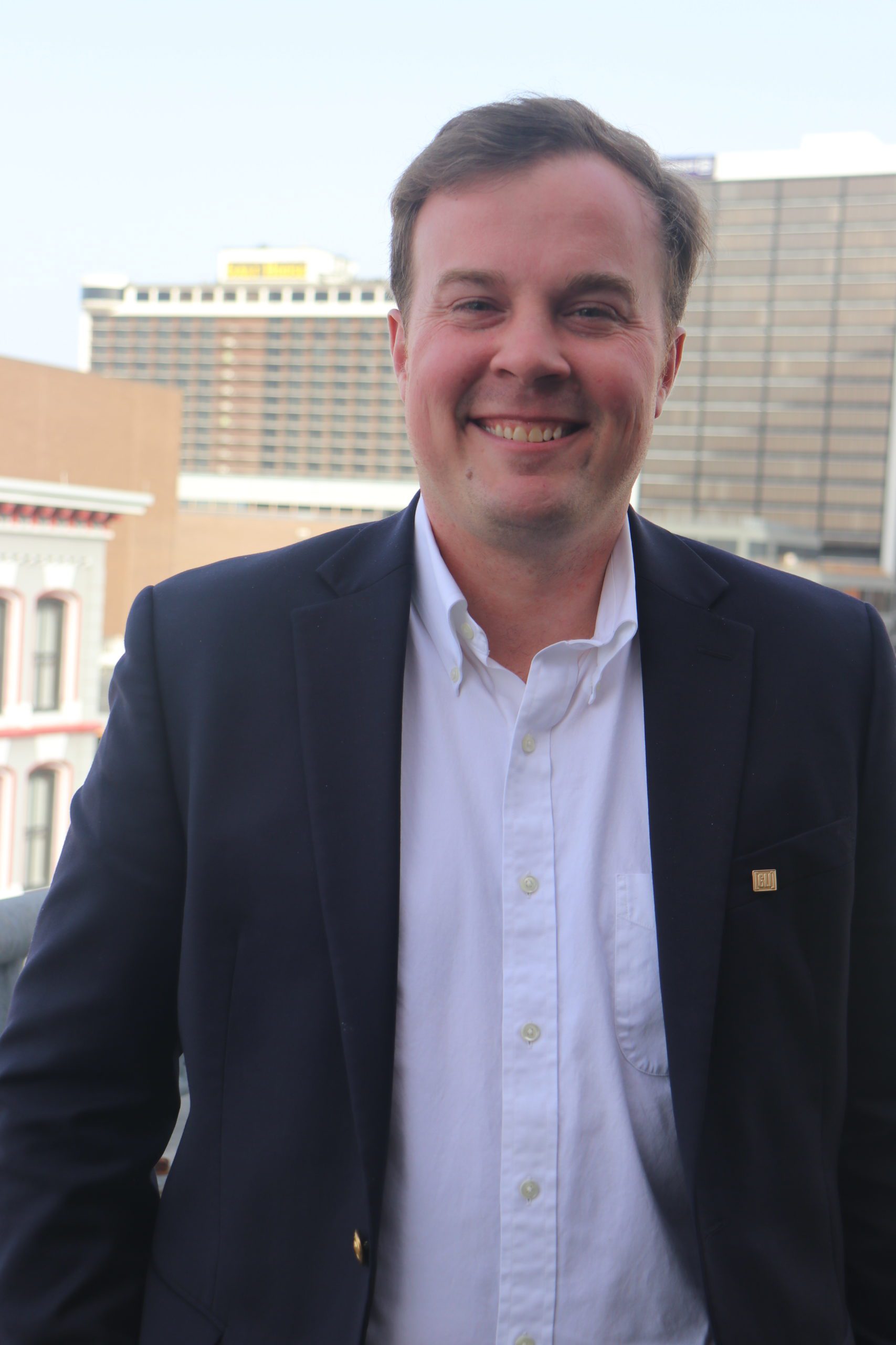 Headshot of Clark Welch wearing an unbuttoned black suit jacket and white shirt with open collar.