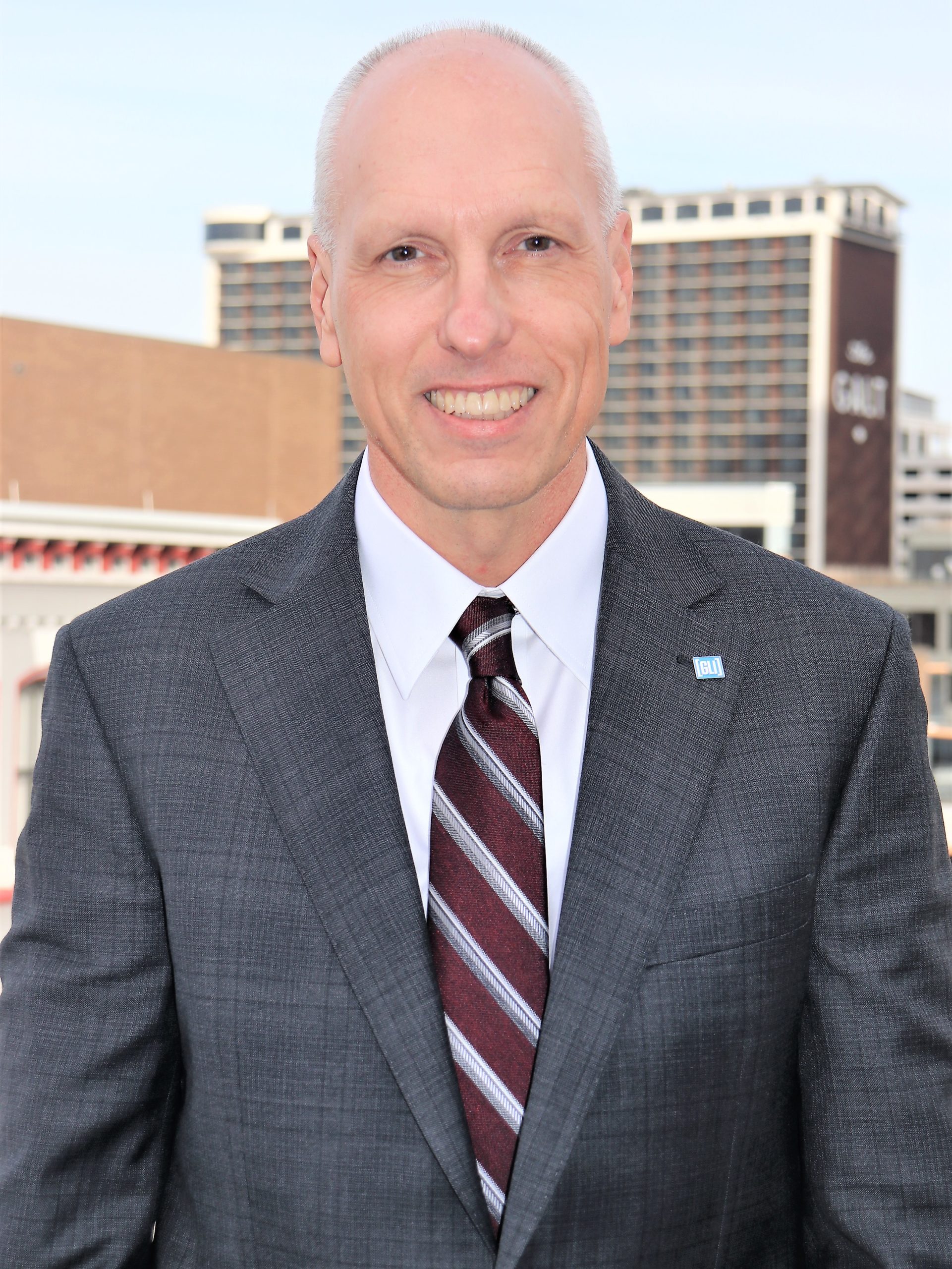 headshot of Dean Schlader wearing a gray suit and striped tie.