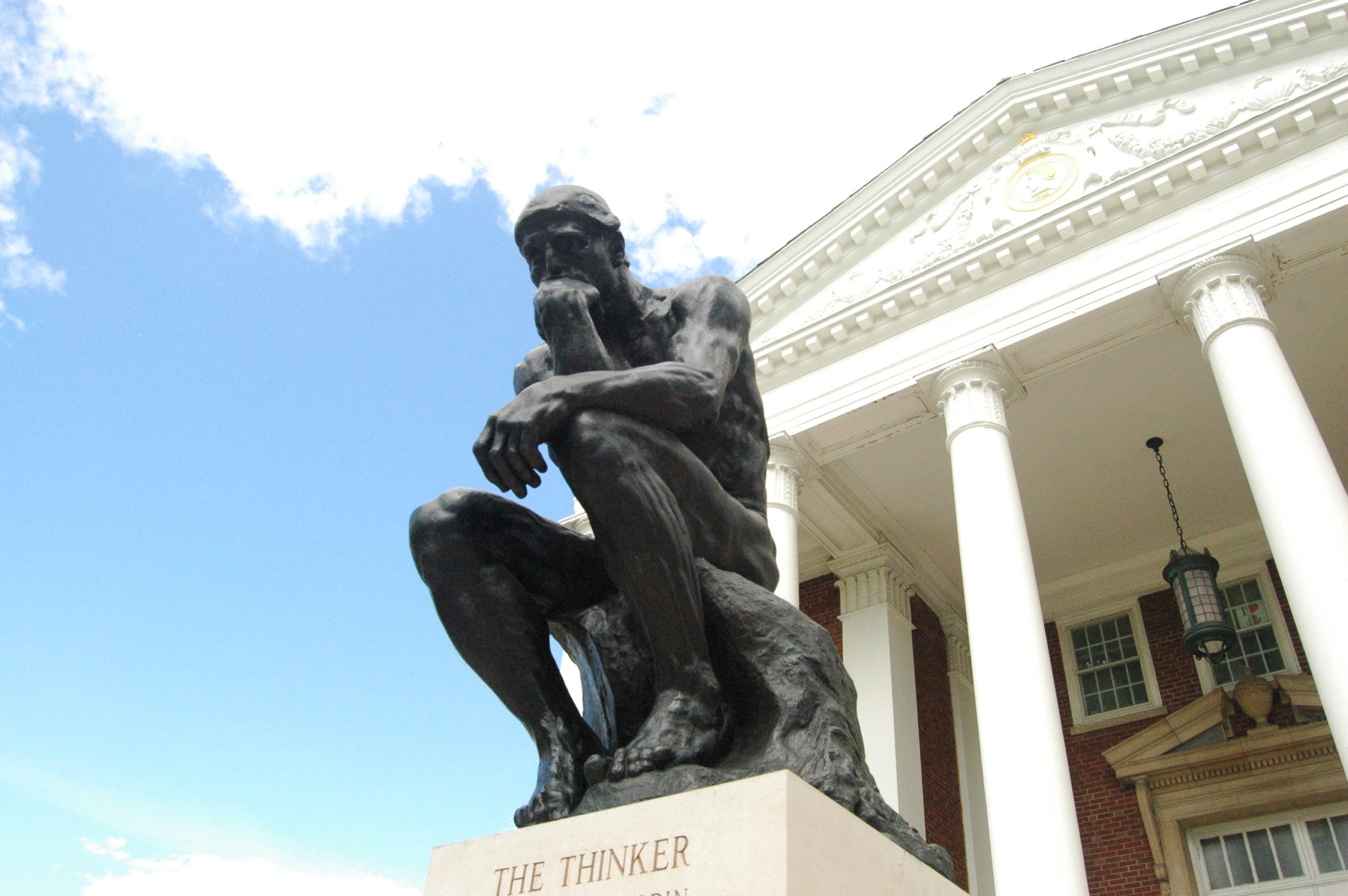 The Thinker statue against a blue sky and white-columned structure